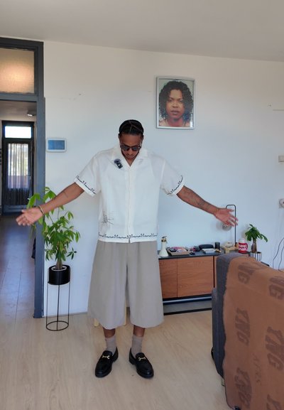 Camisa blanca de manga corta con bordado negro, combinada con pantalones cortos beige hasta la rodilla. Los accesorios incluyen calcetines marrones y mocasines negros.