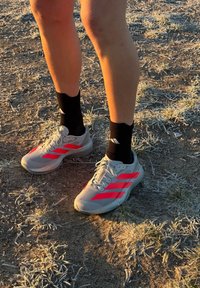 Gambe che indossano scarpe da corsa Adidas bianche e rosse con calzini neri, in piedi su erba secca e ghiacciata e terra all'alba o al tramonto.
