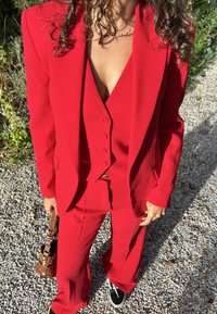 Sarkans piegriezts uzvalks ar struktūrētu žaketi, atbilstošu veste ar pogām un izpletušos bikses. Papildināts ar fakturētu brūnu rokassomu.