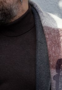 Harmaa villasekoitetakki, jossa viininpunainen ja harmaa ruututettu kuvio, kerroksittain päällä tummanruskea poolokauluspaita. Yksityiskohtina sivutasku ja teksturoitu kangas.