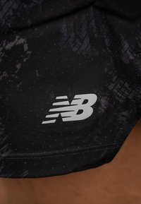 Čierne športové šortky s textúrovaným vzorom, vybavené perforáciami pre ventiláciu a sivým logom "NB" na spodnej časti nohy.