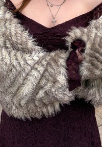 Egy burgundi csipkeruhát viselő nő, akinek két arany nyaklánc van a nyakában, az egyik kereszt medállal, és egy textúrált szürke prémkendővel van bugyolálva.