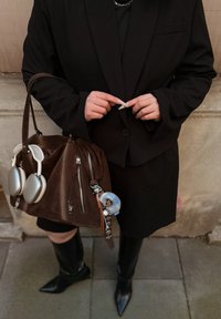 Brun veske i semsket skinn med sølvdetaljer, sideskipper og et anheng; svarte spisse støvletter som går til ankelen; formelt svart antrekk.