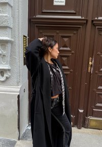 Sort lang frakke over en kort sort top og ternet skjorte, kombineret med sorte jeans. Brun dør med diamantmønstre og messingbeslag.