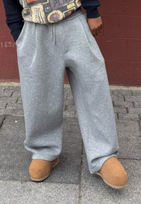 Pantalon de survêtement gris clair à jambes larges avec une taille à cordon, doté de poches latérales profondes, associé à des bottines marron clair en simili daim à enfiler.