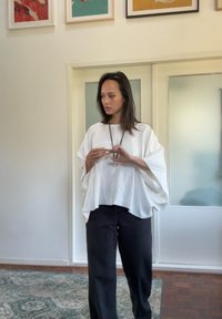 Voľné biele tričko s krídlovými rukávmi, skombinované s čiernymi nohavicami. Hladká textúra, neutrálny farebný paleta, minimalistický dizajn.