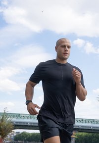 Musthave mustern t-särk, lühikeste varrukatega, ümar kaelus, subtillise logo detailiga; koos mustade lühikeste pükstega, helesinise taeva taustal.