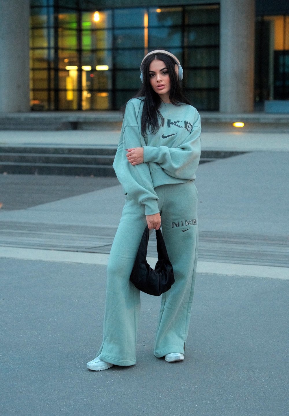 Mintgrønn Nike sweatshirt og matchende joggebukser med store logo-detajer. Modellen holder en svart bag og har på seg sølvhodetelefoner. Casual gatekultur.