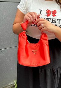 Rød nylon håndtaske med en afslappet design, præget af et trekantet logo, sølvdetaljer og et knyttet håndtag. Lynlåsåbning øverst.