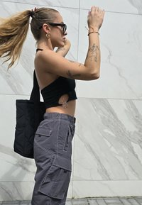 Μαύρο cropped τοπ με κοπές, γκρι cargo παντελόνι με πολλές τσέπες και μια μαύρη παπλωμένη τσάντα. Μακριά μαλλιά μαζεμένα πίσω.