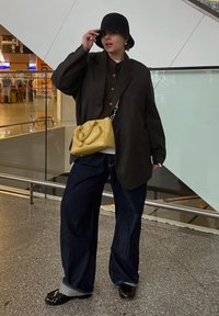 Overdimensjonert svart blazer over en brun genser, vide blå jeans og svarte sko. Tilbehør i form av en gul håndveske og svart hatt.