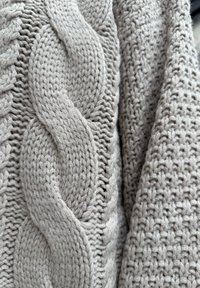 Gros plan sur un tissu tricoté épais de couleur crème présentant un large motif torsadé à côté d'un motif tricoté texturé.