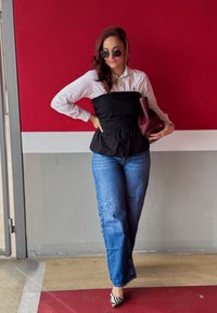Czarny top peplum na białej koszuli z długim rękawem, w połączeniu z niebieskimi spodniami o szerokich nogawkach i czarno-białymi szpilkami w paski. Akcent w postaci burgundowej torebki.