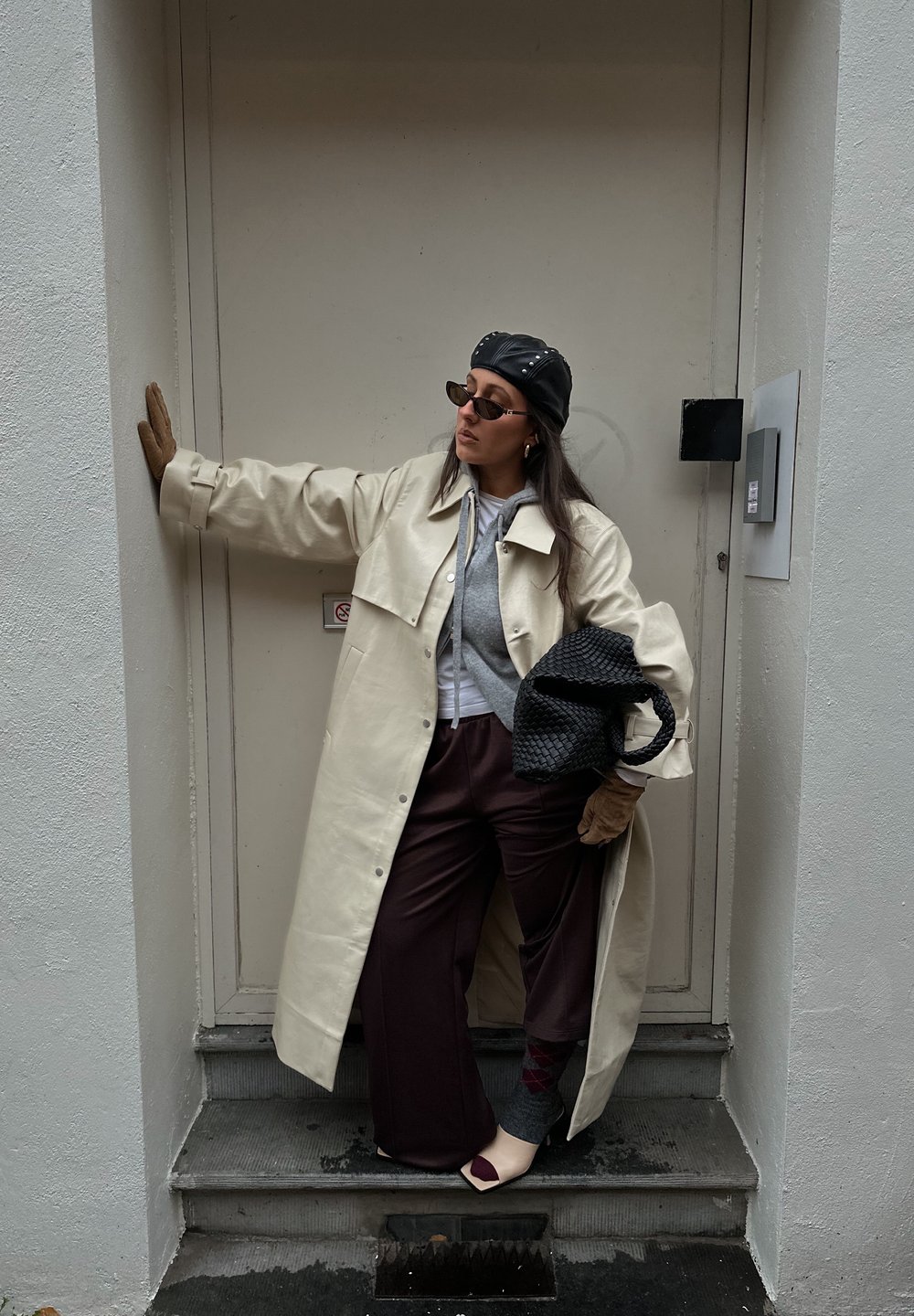 Manteau oversize couleur crème, sweat à capuche gris, pantalon large bordeaux, chaussettes à motifs, gants, sac à main noir, lunettes de soleil foncées et casquette noire.
