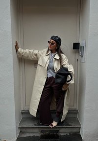 Manteau oversize couleur crème, sweat à capuche gris, pantalon large bordeaux, chaussettes à motifs, gants, sac à main noir, lunettes de soleil foncées et casquette noire.