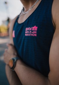 Mörkblå linne med en texturerad mönster, med en ljusrosa "BMW Berlin Marathon" logotyp på bröstet. Accentuerad med en silverfärgad klocka.