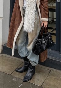 Rudas kailio imitacijos pamušalu paltas, baltas tekstūruotas šalikas, išblukę mėlyni platūs džinsai, juoda odinė rankinė su sidabrine įranga ir juodi smailūs ankletai.