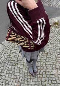 Bordeauxrød sportjakke med hvide striber, dyreprint håndtaske, grå ternet nederdel, grå knæstrømper og bordeauxrøde spidse hæle.