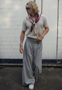 Világosszürke, bőszárú nadrág magas derékkal, amelyhez egy rövid, fehér perforált kötött felsőt és nyaknál megkötött mintás sálat visel.