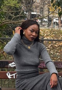 Sivý rebrovaný rolák v kombinácii so zodpovedajúcou sivou suk�ňou. Zlaté ozdoby zahŕňajú reťazový náhrdelník a veľké náušnice.