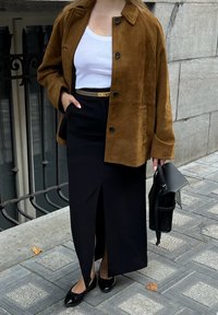 Pruun nubukist jakk, valge topp, must seelik külglõikega, mustad lamekingad, hoides musta kotti. Tekstuuriga kangas ja kohandatud disaini detailid.