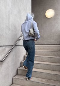 Huppari harmaana, siniset leveälahkeiset farkut ja valkoiset korokepopot. Pieni vaalea harmaa laukku on heitetty olkapäältä, kun noustaan betoniporrasta ylös.