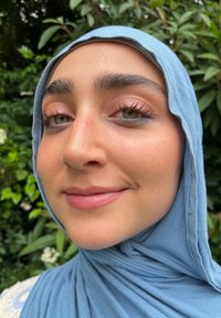Lyseblå hijab henger rundt ansiktet, som komplementerer myke hudtoner. Personen har grønne øyne med lys sminke og naturlige vipper.