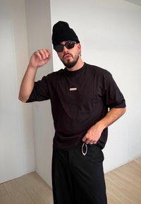 Fekete, túlságosan nagy fekete póló kis piros logóval, laza fekete nadrággal párosítva. Kiegészítők: fekete sapka és napszemüveg. Ezüst színű fém részletek.