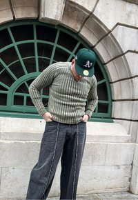 Green striped sweater with a ribbed texture, paired with wide-leg black jeans featuring distressed seams. A green cap completes the look.