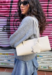 White leather handbag with a rectangular shape, featuring a flower-shaped tag. The bag has double handles and a matte finish.