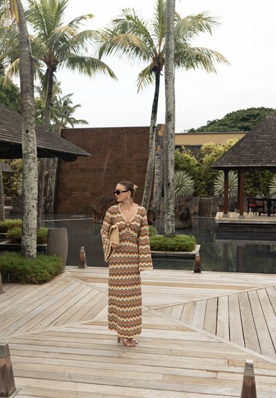 Vestido maxi largo y estampado en tonos cálidos y terrenales con un diseño de zigzag; cuenta con mangas acampanadas, un escote profundo y una silueta fluida.