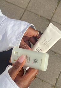 Deux produits de soin de la peau : un bâton tournant vert pâle et un tube de crème, tous deux au design minimaliste et avec des textes en coréen, tenus dans une main à la peau claire.