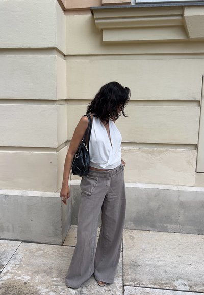 Top blanco sin mangas con un escote en V profundo, combinado con pantalones de pierna ancha gris claro y un bolso negro pequeño. Pared texturizada de fondo.