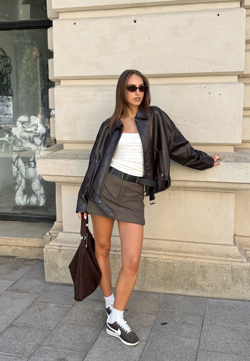 Black leather bomber jacket, white tank top, striped grey mini skirt, dark brown bag, white socks, and dark trainers with a light sole.