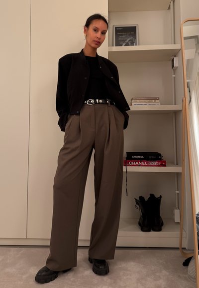 Chaqueta bomber negra, top ajustado negro, pantalones beige con pliegues, zapatos de plataforma negros y gruesos; los accesorios incluyen un cinturón plateado y pendientes.