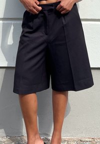 Shorts neri a gamba larga realizzati in tessuto testurizzato, con vita alta e pieghe frontali, dal taglio morbido e alla lunghezza del ginocchio.