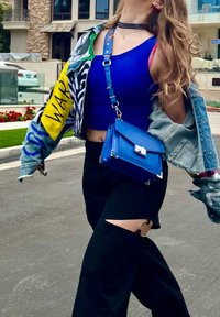 Denim jacket with colorful patches, blue crop top, black wide-leg pants with cutouts, and a small blue crossbody bag with silver hardware.