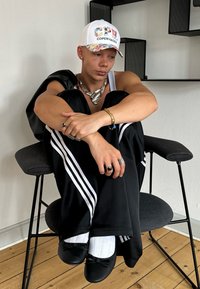 Juodos sportinės kelnės su baltais dryžiais, balta kepurė su tekstu "COPEN HAGEN", sidabrinė stiliaus kaklo papuošalas ir juodi baletki.