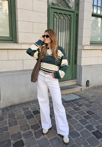 Polo de rayas verde y crema de manga larga, pantalones anchos blancos, bolsa de mimbre marrón y zapatillas ligeras sobre una acera de piedra.