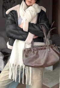 Jachetă din piele neagră cu căptușeală bej din blană, eșarfă albă cu franjuri și geantă maro din piele. Ținuta prezintă culori și texturi discrete.