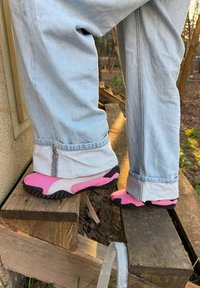 Rózsaszín és szürke dizájnú sportcipők, texturált gumitalppal és jellegzetes fekete részletekkel. Világoskék farmernadrággal párosítva.