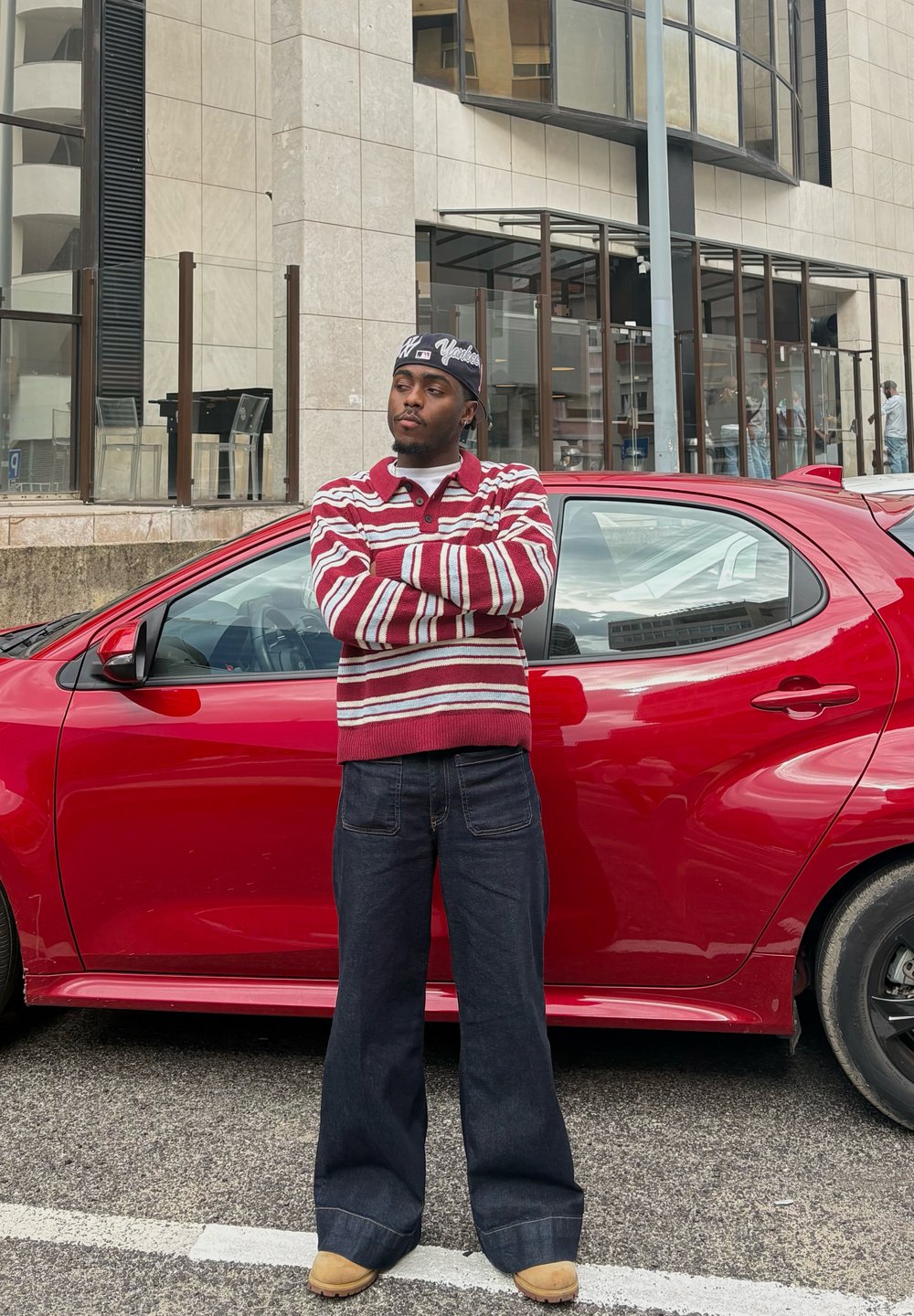 Red-striped jumper with a collar, dark blue wide-leg jeans, and tan boots. Standing beside a red car in an urban setting.