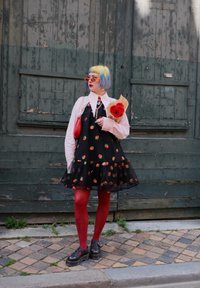 Robe noire avec motif de fraises, ourlet en volants superposés, associée à une chemise blanche à col, des collants rouges et des chaussures à plateforme. Les accessoires comprennent un sac rouge et des fleurs.