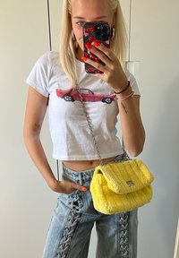 Κίτρινη χνουδωτή τσάντα με καπιτονέ σχέδιο και ασημένια αλυσίδα. Φοριέται με λευκό κοντό μπλουζάκι και ανοιχτόχρωμα τζιν με κορδόνια.