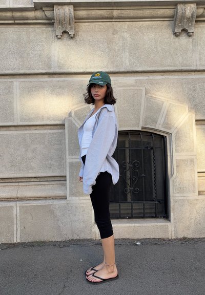 Camisa de botones de gran tamaño a rayas, camiseta sin mangas blanca, leggings negros, gorra verde, chanclas; con texturas suaves y un diseño casual.