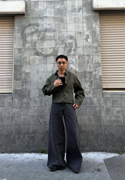Camisa verde de cropped con botones, top negro ajustado, pantalones vaqueros anchos de denim gris oscuro y zapatos negros. Los acentos de joyería de plata completan el conjunto.