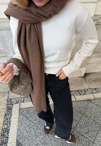 Striket creme trøje, brun uld tørklæde, sorte videre ben jeans, vævet olivengrøn taske, brune sneakers og guld ringe.