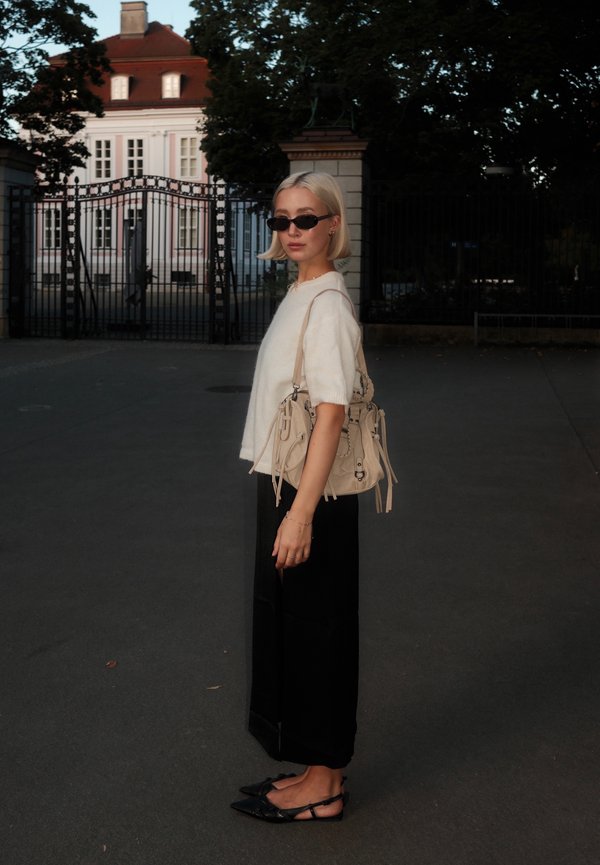 Bēša rokassoma ar šķipsnām, pārmērīgi lieli melni bikses, baltā džemperis un melni saulesbrilles. Gludi materiāli un minimālistisks dizains.