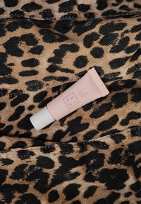 Pink tube til øjenskyggeprimer med hvid hætte, hvilende på leopardprintet stof med sorte og brune pletter. Glat tekstur, minimal branding.