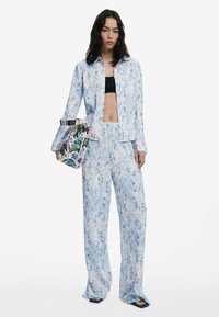 Blommönstrad koordinerad outfit med en ljusblå skjorta och vida byxor. Tyget har en mjuk textur med ett färgglatt mönster.